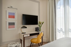 Una habitación de hotel con cama, escritorio, silla, televisión y una obra de arte en la pared.