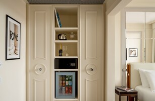 A room with a minibar, a framed picture on the wall, and a bed with a white pillow.