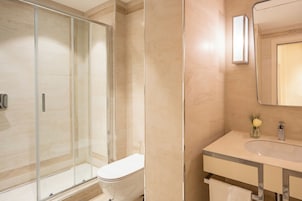 A modern bathroom with a glass-enclosed shower, a white toilet, and a vanity with a mirror and a small vase of flowers.