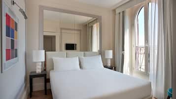 Ein Hotelzimmer mit einem großen Bett, zwei Nachttischen mit Lampen, einem Fernseher und einem Balkon mit Vorhängen.