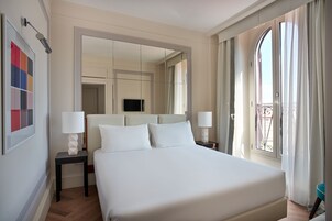 Ein Hotelzimmer mit einem großen Bett, zwei Nachttischen mit Lampen, einem Fernseher und einem Balkon mit Vorhängen.