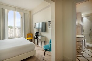A hotel room with a bed, a desk with a chair, a television, and a bathroom with a shower.