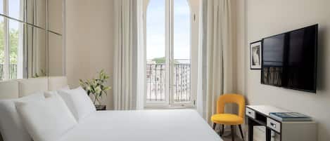 A hotel room with a bed, a desk, a chair, a TV, and a balcony with curtains.