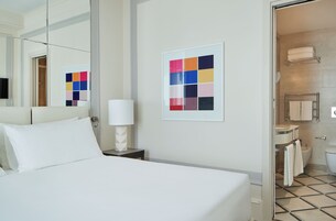 Camera d'albergo con un letto, un comodino con una lampada, un bagno con il water, lavandino e portasciugamani.