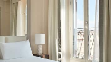 Quarto de hotel com uma cama grande, mesa de cabeceira com abajur, janela com cortinas e varanda com guarda-corpo.