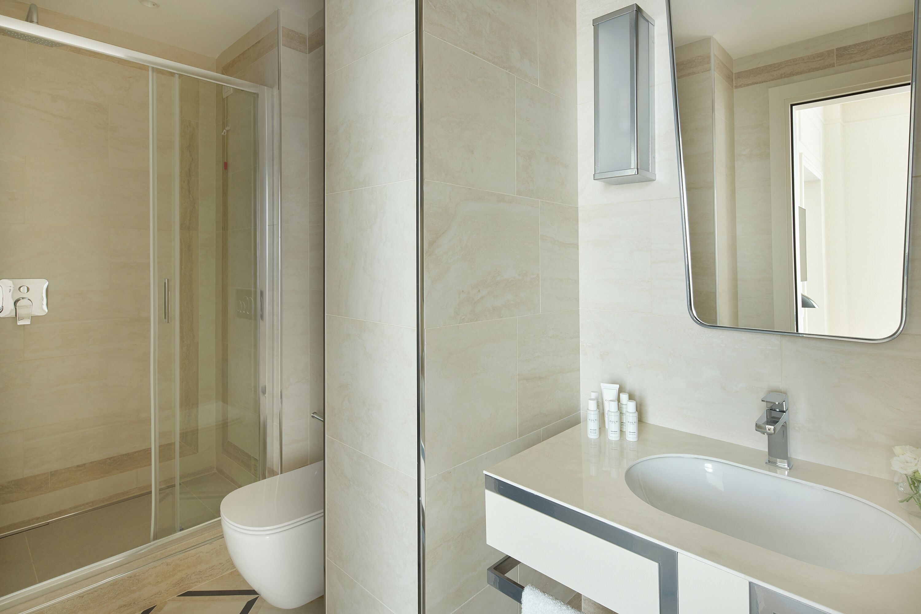 Un bany modern amb una cabina de dutxa de vidre, un lavabo blanc i un mirall sobre el lavabo.