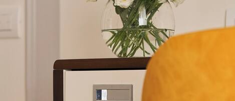 A room with a wooden nightstand, a vase with white flowers, and a yellow chair.