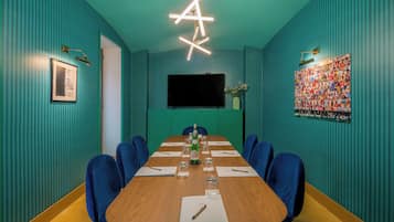 Uma sala de conferências com uma mesa comprida, cadeiras azuis, uma tela de projetor e um cartaz grande na parede.
