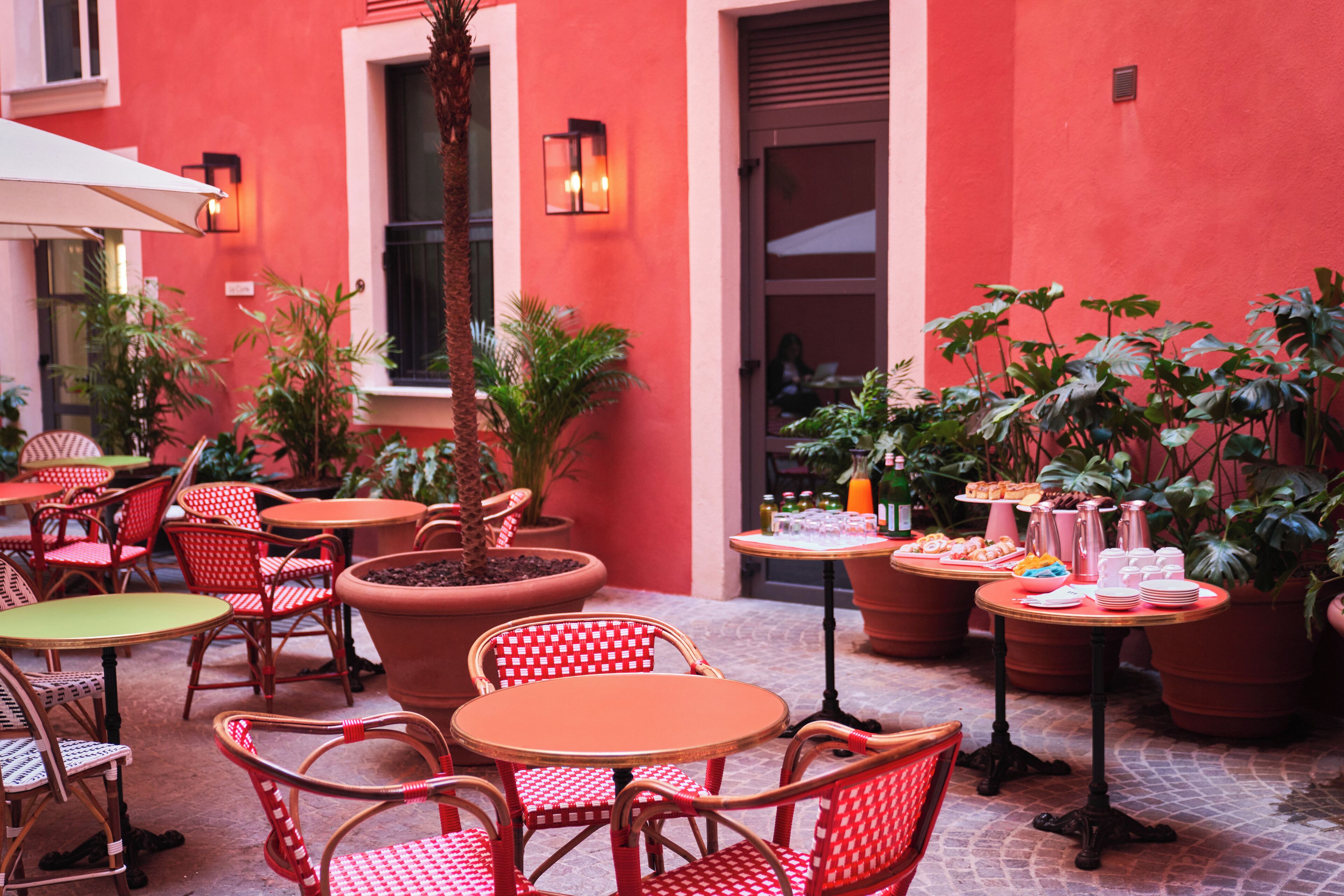 An outdoor café with red and white checkered chairs, terracotta pots, and a variety of food and drink items on a table.