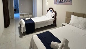 Habitación de hotel con dos camas, una mesita de noche, una lámpara de pared y una puerta que da a otra habitación.
