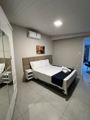 Une chambre d’hôtel comprenant un lit, une table de chevet, un miroir, un appareil de climatisation et un tableau au mur.