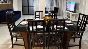 Un comedor con una mesa negra y sillas de madera, un televisor sobre un soporte blanco, y un sofá azul al fondo.