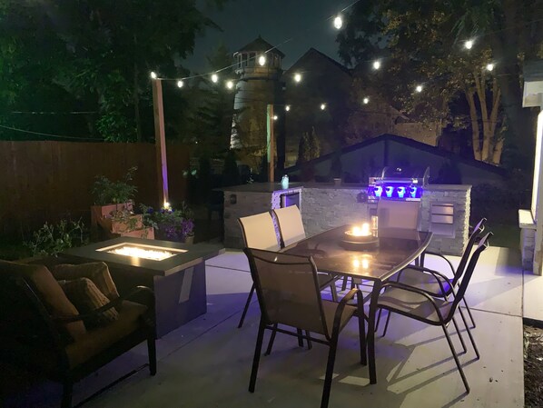 Un patio al aire libre con mesa, sillas y una parrilla integrada.