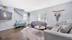 Een moderne woonkamer met een trap, een grijze bank, een blauwe fauteuil en een relaxstoel.
