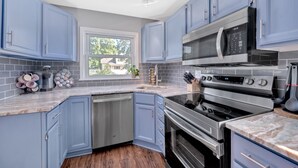 Een moderne keuken met blauwe kastjes, roestvrijstalen apparatuur en een raam dat natuurlijk licht binnenlaat.