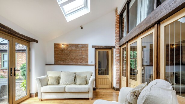 Une pièce spacieuse avec un plancher en bois, un canapé blanc et une porte vitrée donnant sur l’extérieur.
