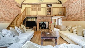 Un vaste espace de vie doté d’un haut plafond, de poutres apparentes en bois, d’une cheminée en briques, d’un téléviseur et d’un escalier menant à un niveau supérieur.
