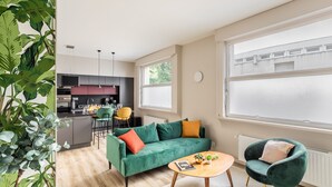 A modern living room with a green sofa, a round coffee table, and a green armchair. There is a kitchen in the background with dark cabinets and a window. - ARNEM - cosy T3 - Two Bedroom Apartment, Sleeps 4 (Rennes)