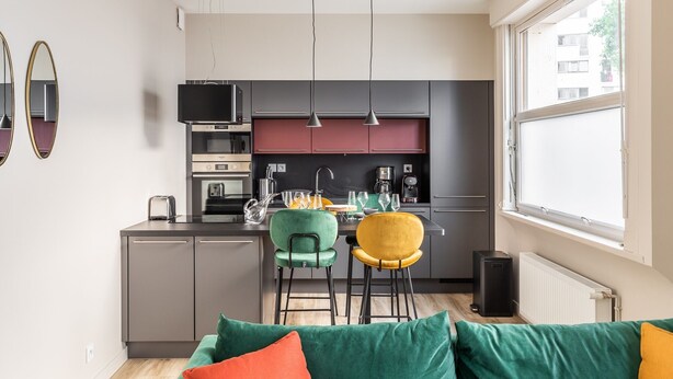 A modern kitchen with a dining area, featuring a central island, pendant lights, and a view of the city through large windows. - ARNEM - cosy T3 - Two Bedroom Apartment, Sleeps 4 (Rennes)