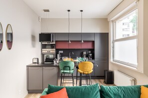 A modern kitchen with a dining area, featuring a central island, pendant lights, and a view of the city through large windows.
