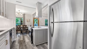 A modern kitchen with white cabinetry, a stainless steel refrigerator, and a dining area with a wooden table and chairs.