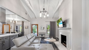 A modern living room with a sectional sofa, a fireplace, a television, and a dining area with a kitchen in the background.