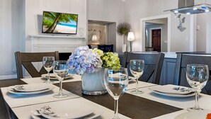 A dining area with a table set for four, a television mounted on the wall, and a decorative plant centerpiece.