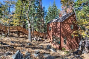 A rustic cabin surrounded by trees with a wooden deck and a stone pathway.