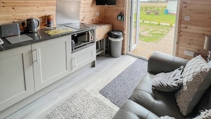 A compact kitchen with a microwave, toaster, and kettle, a grey sofa, and a sliding glass door leading to a garden.