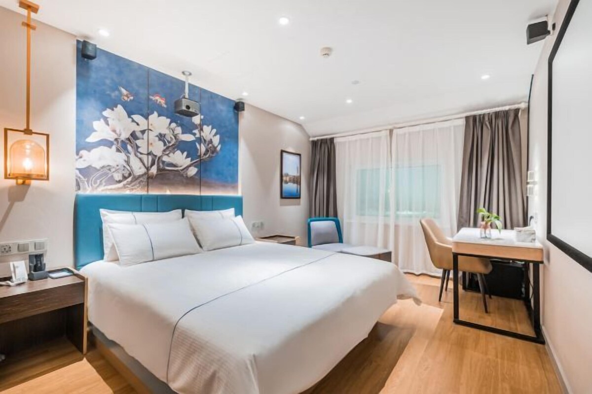 A modern hotel room with a large bed, a desk, and a dining area.