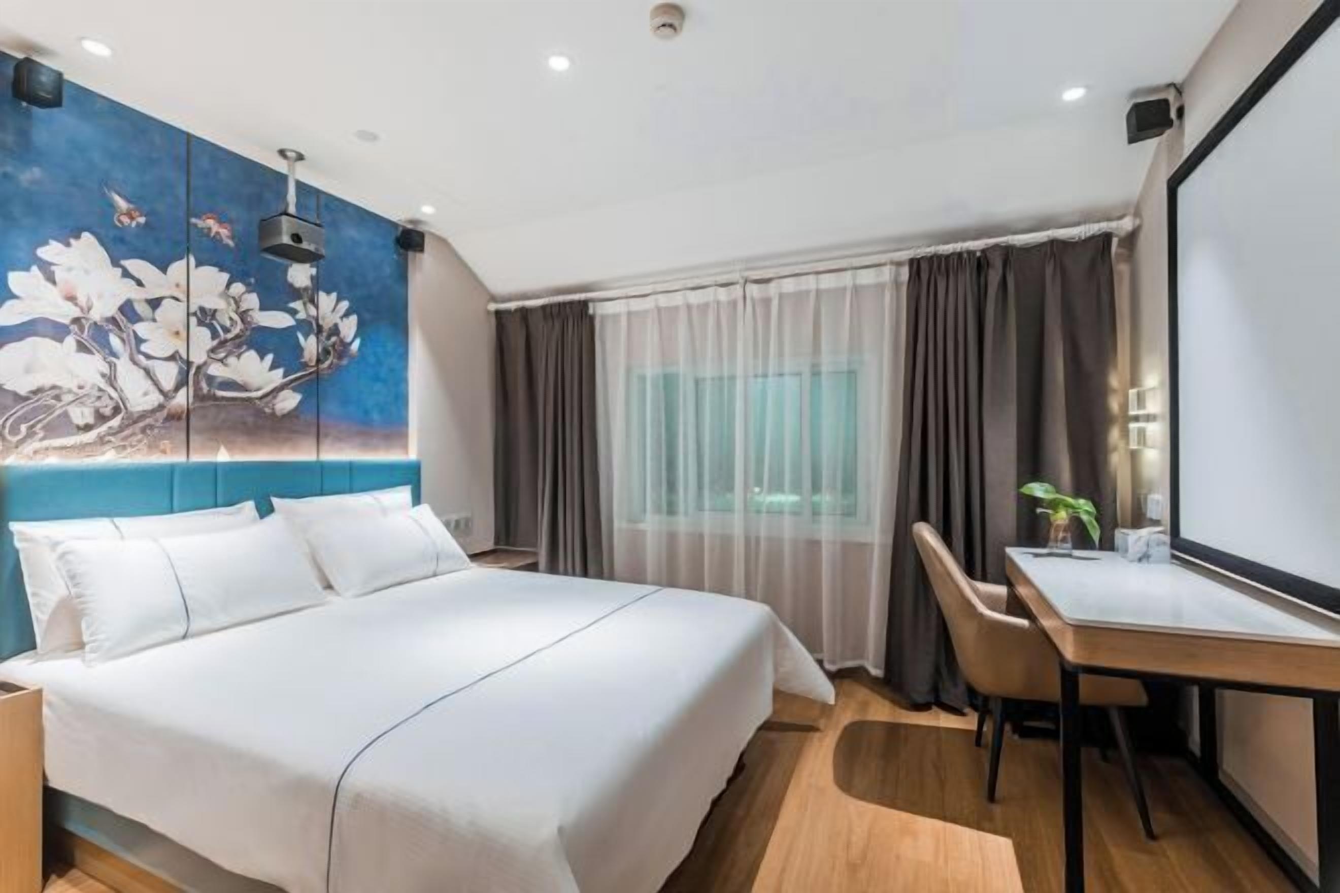 A modern hotel room with a large bed, a desk, and a painting on the wall.