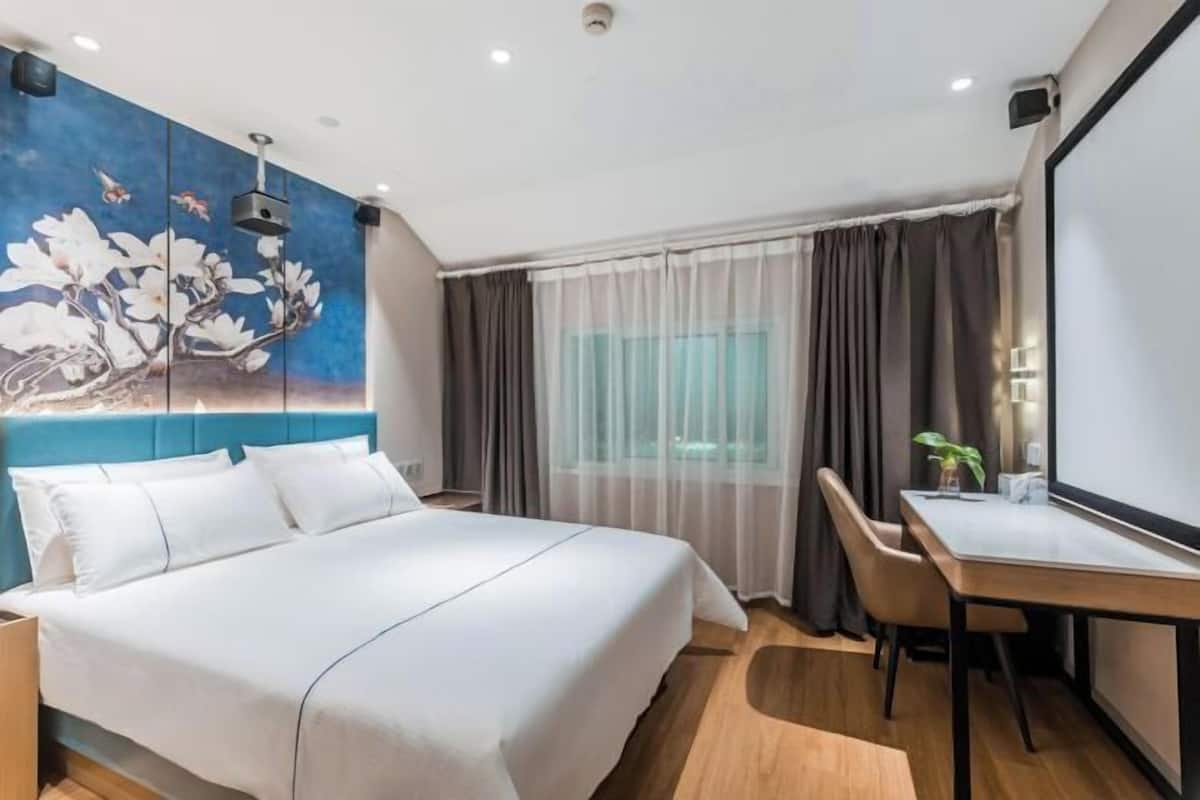 A modern hotel room with a large bed, a desk, and a painting on the wall.