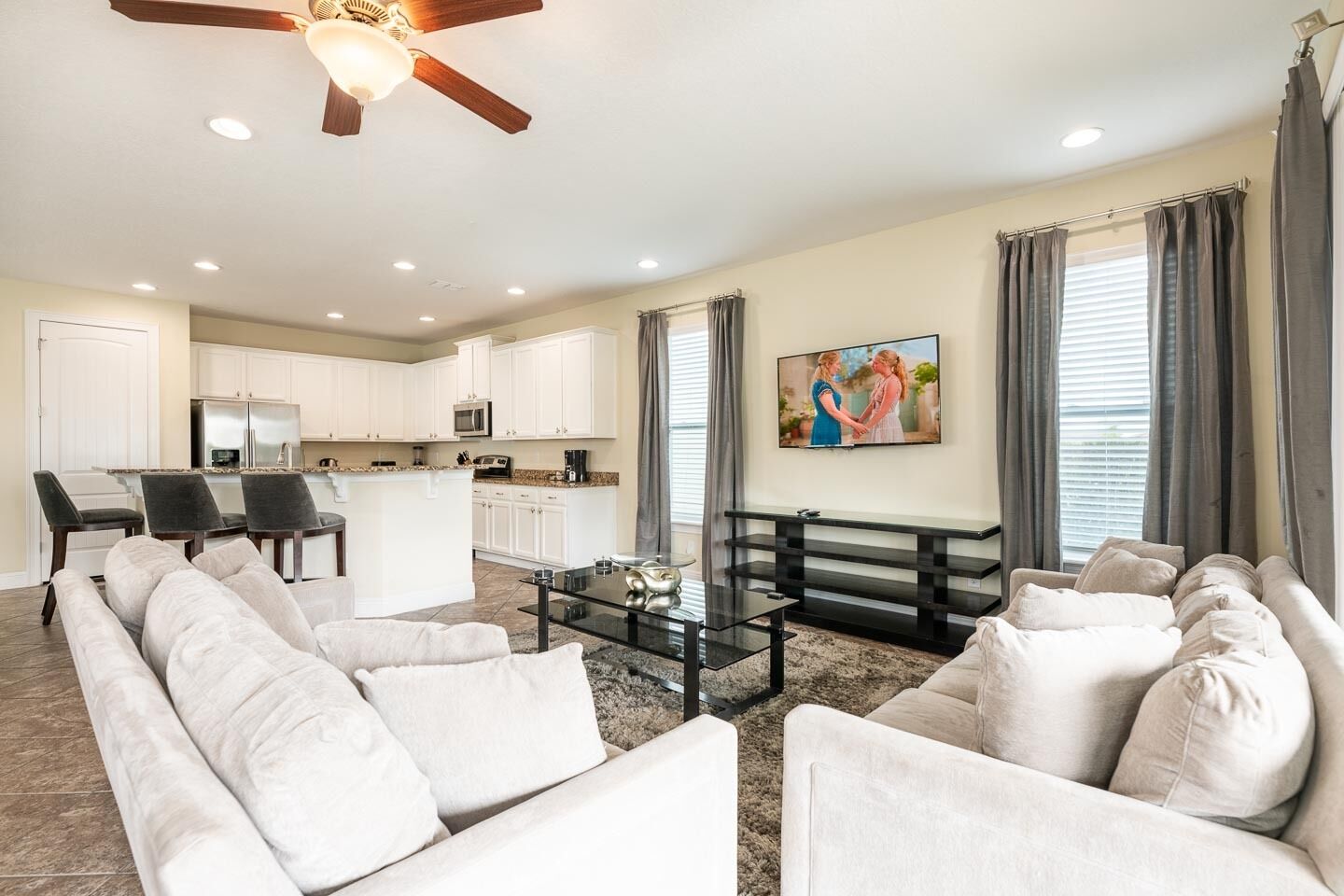 A spacious living room with a sofa set, a coffee table, and a TV mounted on the wall.