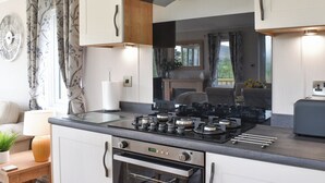 A modern kitchen with a gas stove, oven, and a built-in microwave. There is a window with curtains and a view of greenery outside. - 2 bedroom accommodation in Barrow, near Clitheroe (Barrow, near Clitheroe)