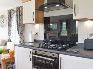 Una cucina moderna con piano cottura a gas, forno e forno a microonde integrato. Si vede una finestra con tende e vista sul verde.