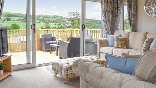 A living room with a sofa, armchair, and a television. There is a sliding glass door leading to a balcony with outdoor furniture. - 2 bedroom accommodation in Barrow, near Clitheroe (Barrow, near Clitheroe)
