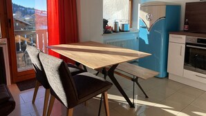Une cuisine moderne avec un réfrigérateur bleu, une table à manger en bois avec des chaises, et une fenêtre donnant sur un paysage enneigé.