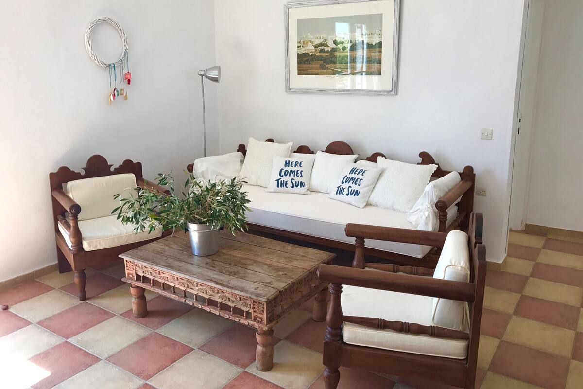 A cozy living room with a wooden sofa, two wooden chairs, a coffee table, and a potted plant.