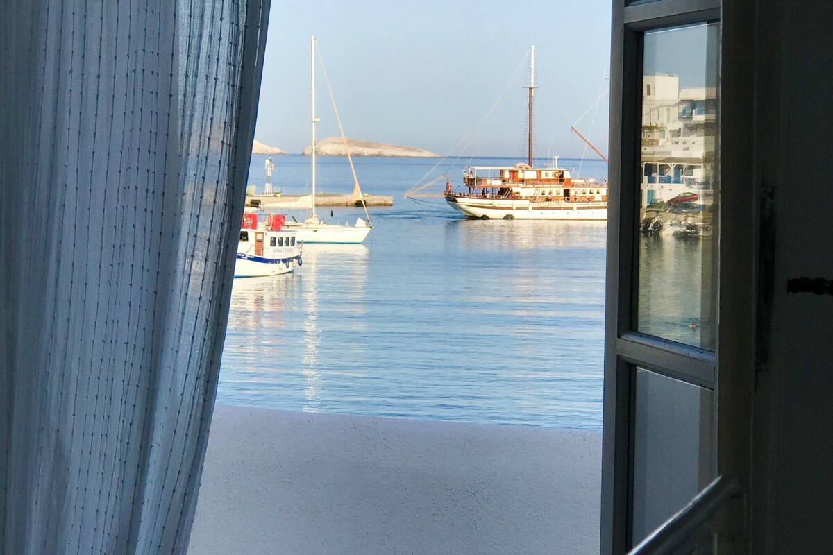 A view from a window overlooking a calm harbor with two boats, one white and one with a red lifebuoy, and a distant landmass.
