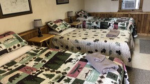 Une chambre avec deux lits, chacun recouvert d’une courtepointe matelassée ornée de motifs représentant des paysages forestiers et des animaux. On y trouve une petite table en bois avec une lampe, ainsi qu’un tableau encadré accroché au mur.