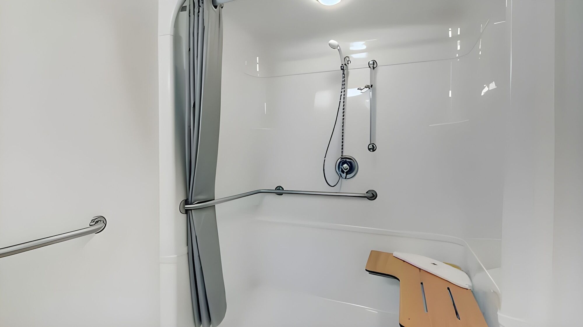 Une salle de bain moderne dotée d’une douche à l’italienne, de barres d’appui et d’un pommeau de douche.
