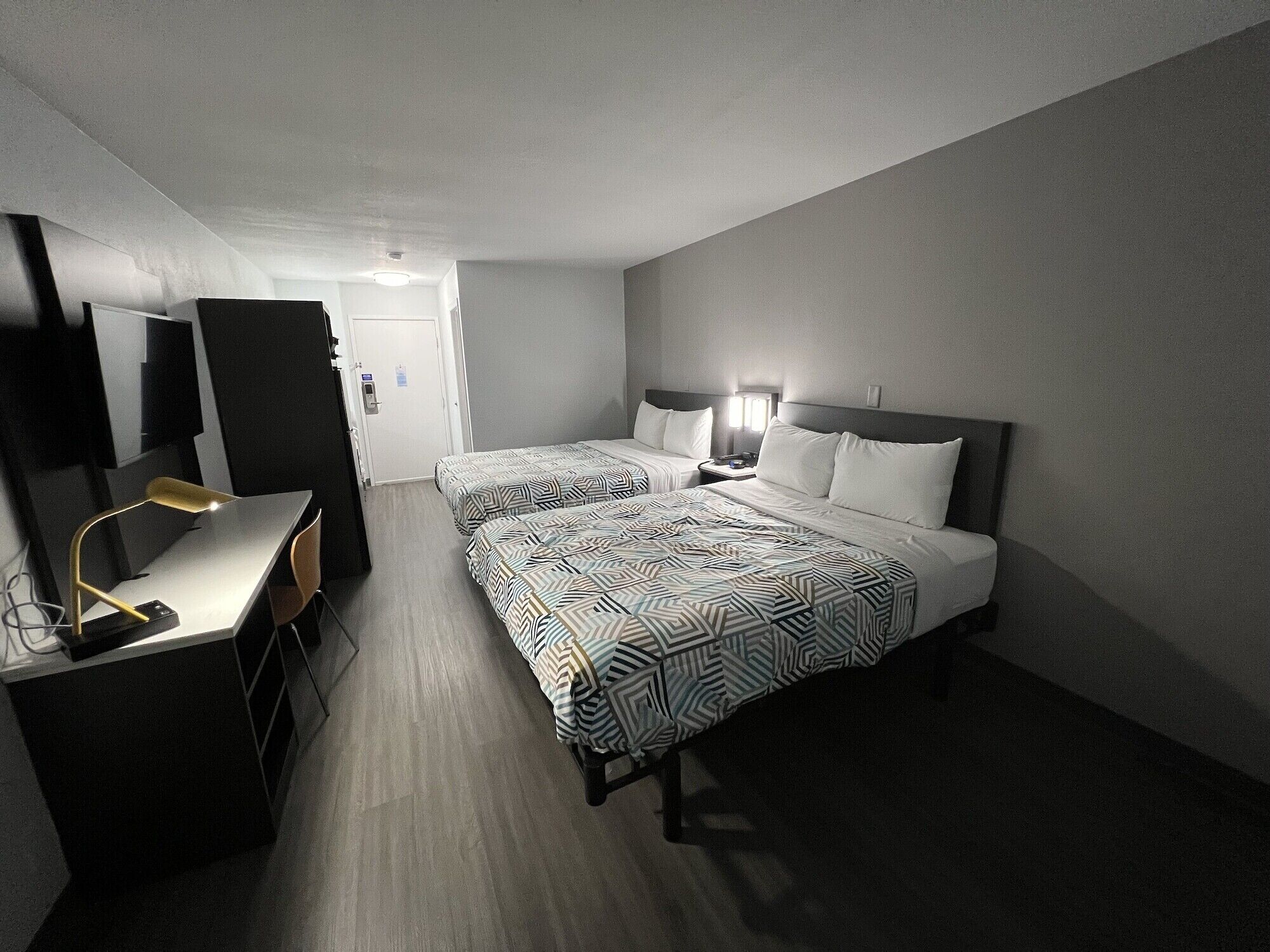 A hotel room with two beds, a desk, a chair, and a TV.