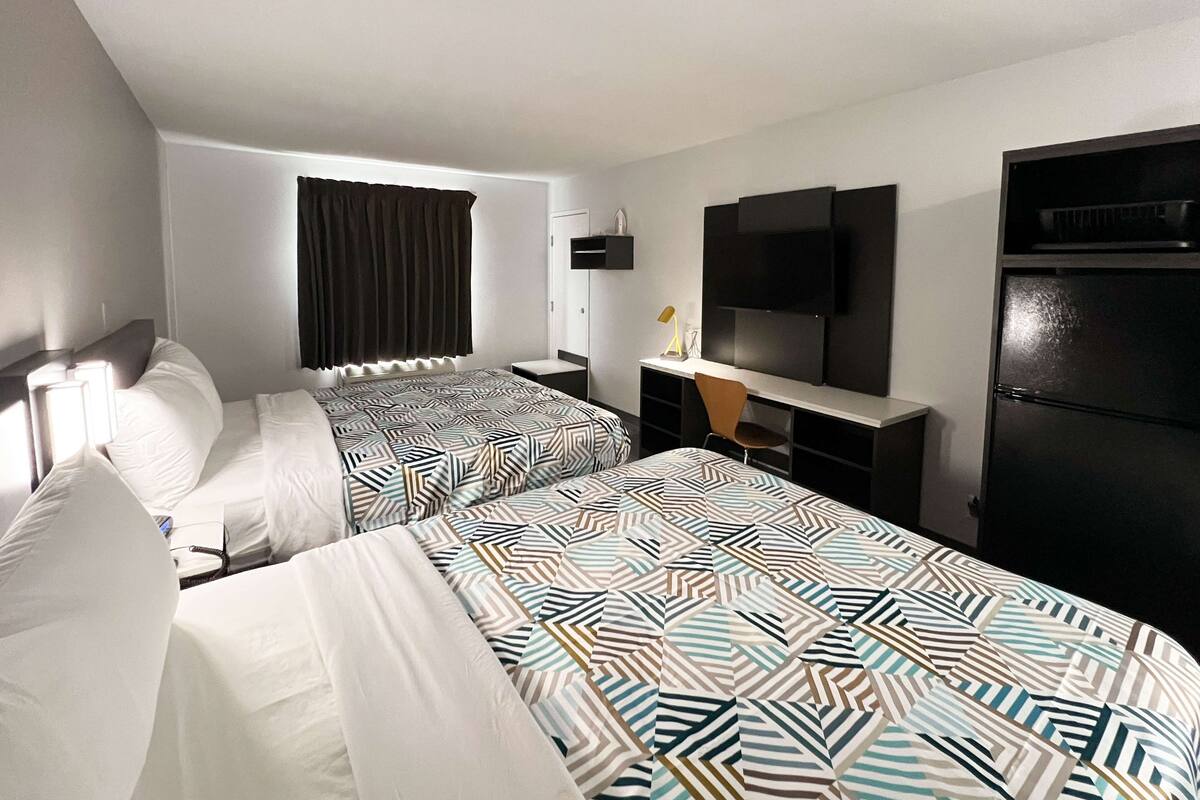 A hotel room with two beds, a desk, a TV, and a refrigerator.