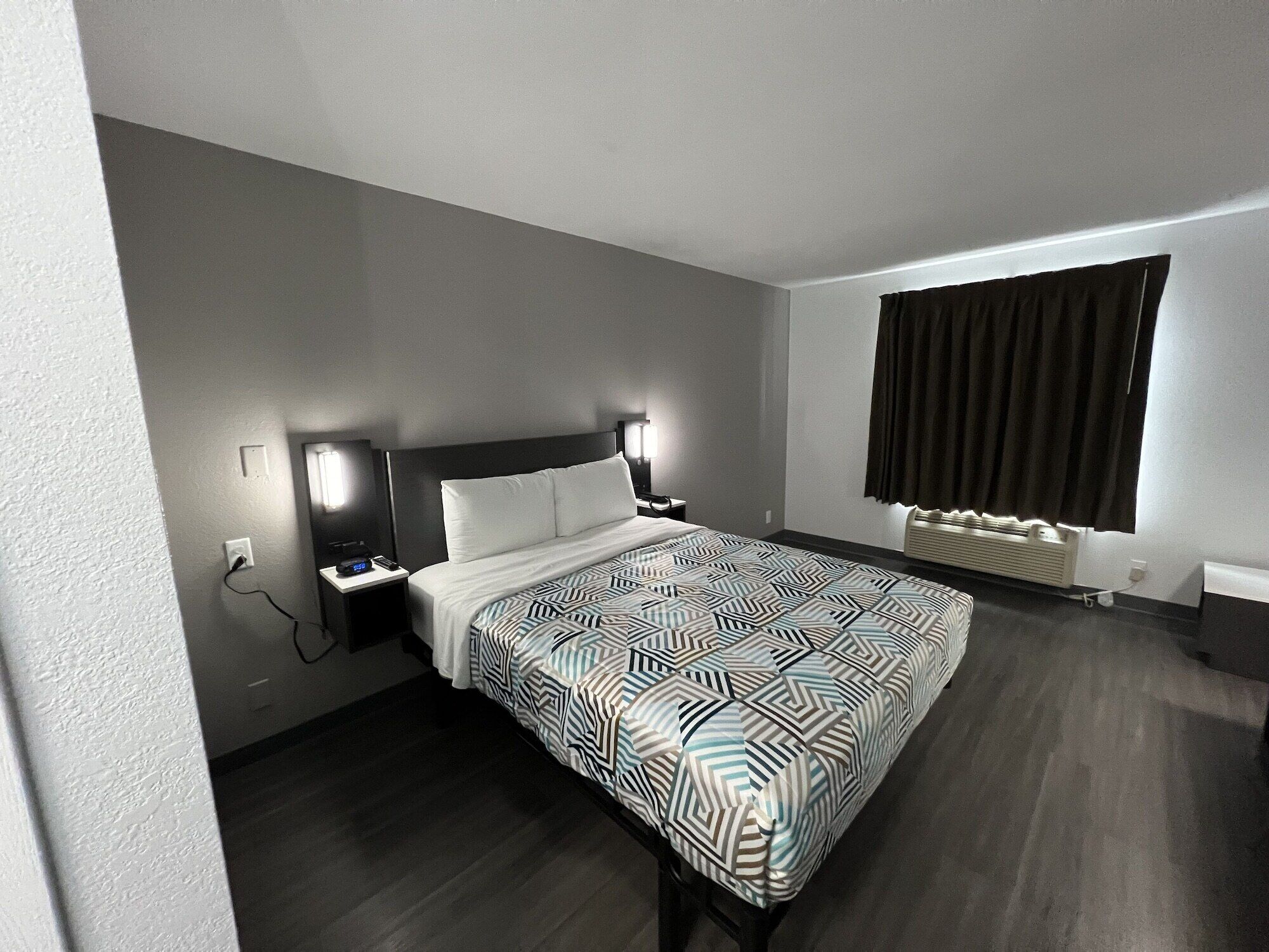 Una habitación de hotel moderna con una cama grande, lámparas de noche, una mesita de noche, una ventana con cortinas y un calefactor incorporado.