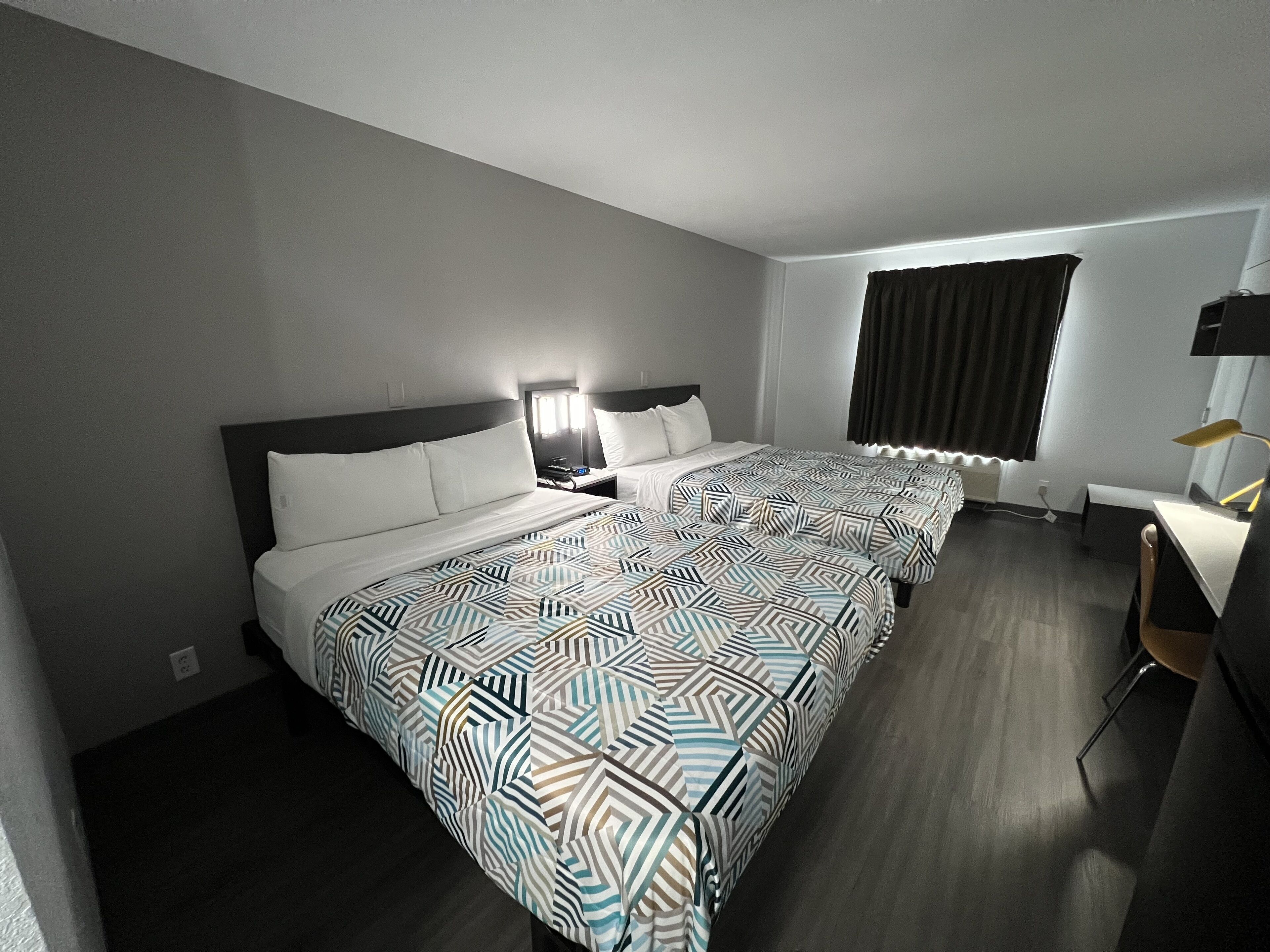Ein Hotelzimmer mit zwei Betten, einem Schreibtisch, einem Stuhl, einer Lampe und einem Fenster mit Vorhängen.