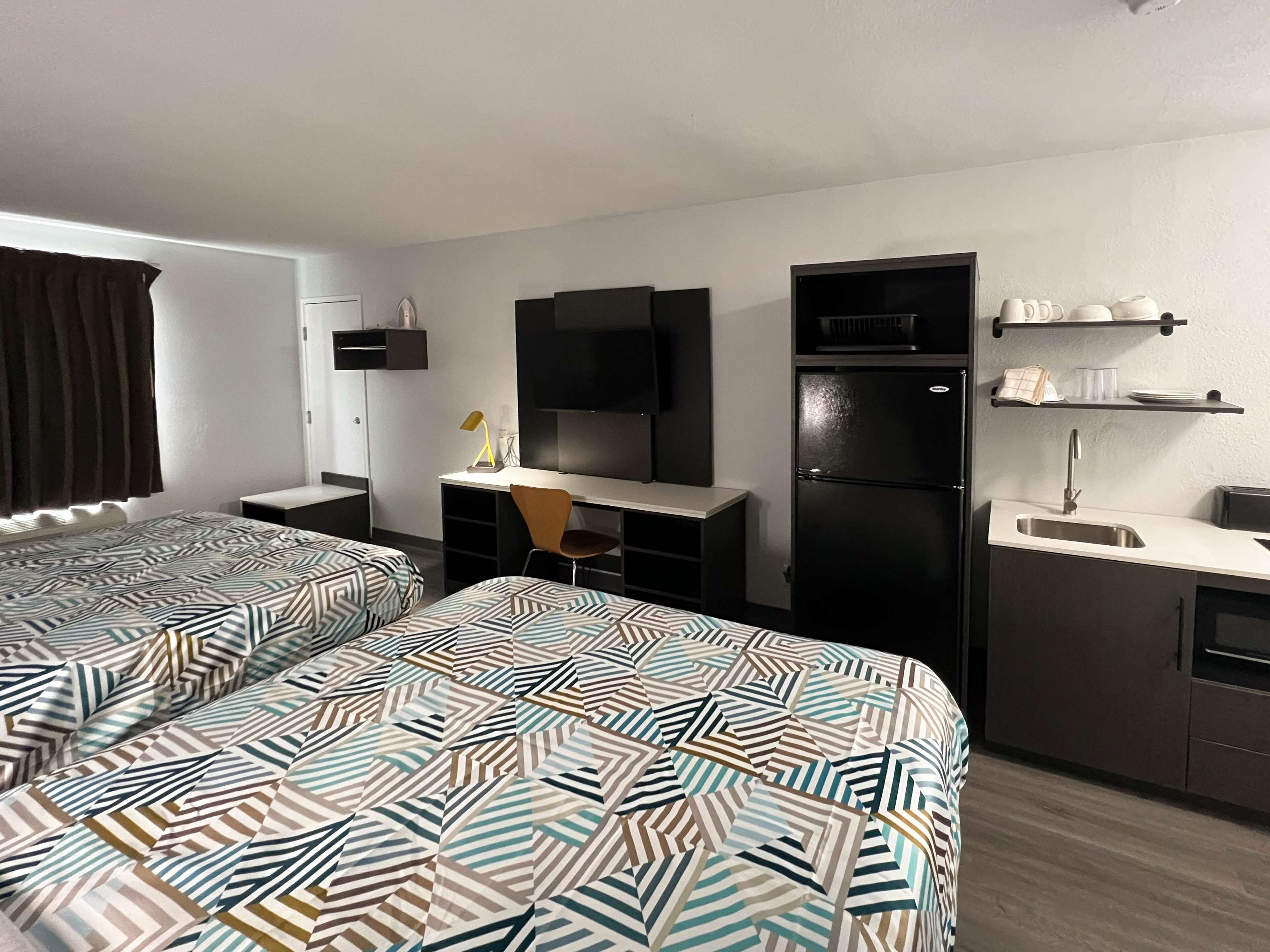 Une chambre d’hôtel avec deux lits, un bureau, une télévision, un réfrigérateur et une kitchenette.