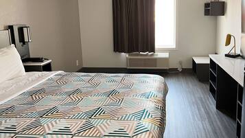 Habitación de hotel con una cama grande, un escritorio, una silla, una ventana con cortinas y un estante en la pared.