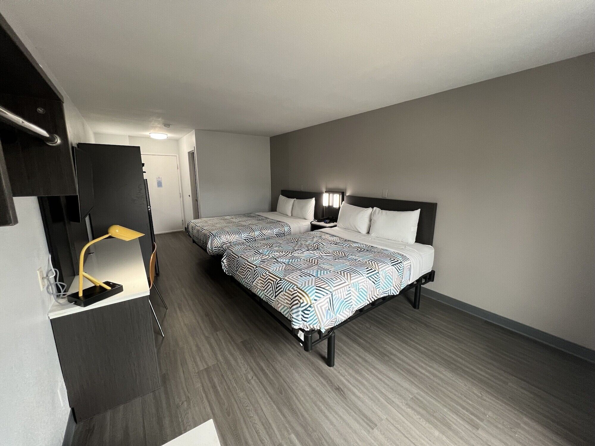 Una habitación de hotel con dos camas, un escritorio con lámpara y un armario.