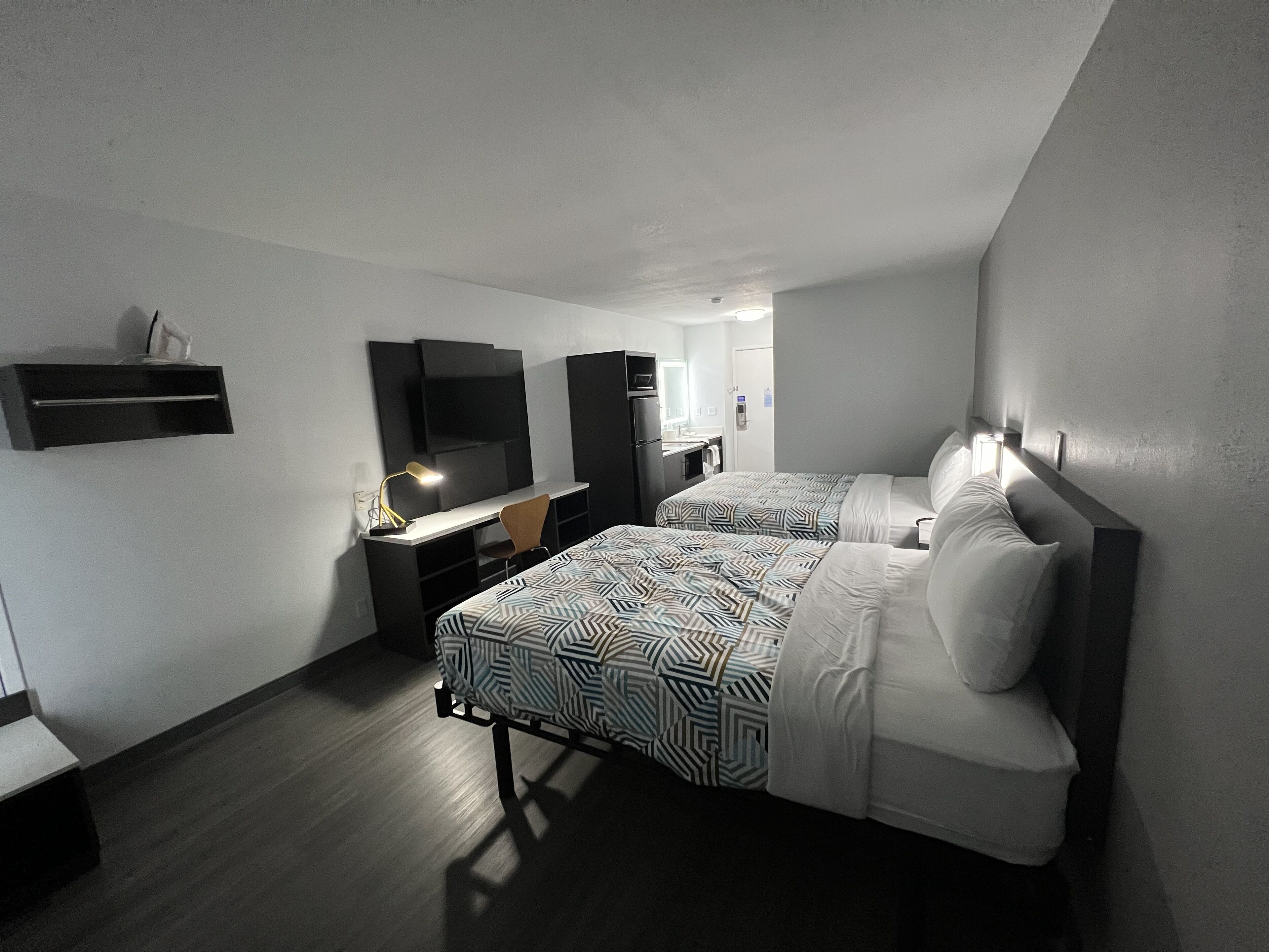 Habitación de hotel con dos camas, un escritorio con silla, un televisor y un espejo.