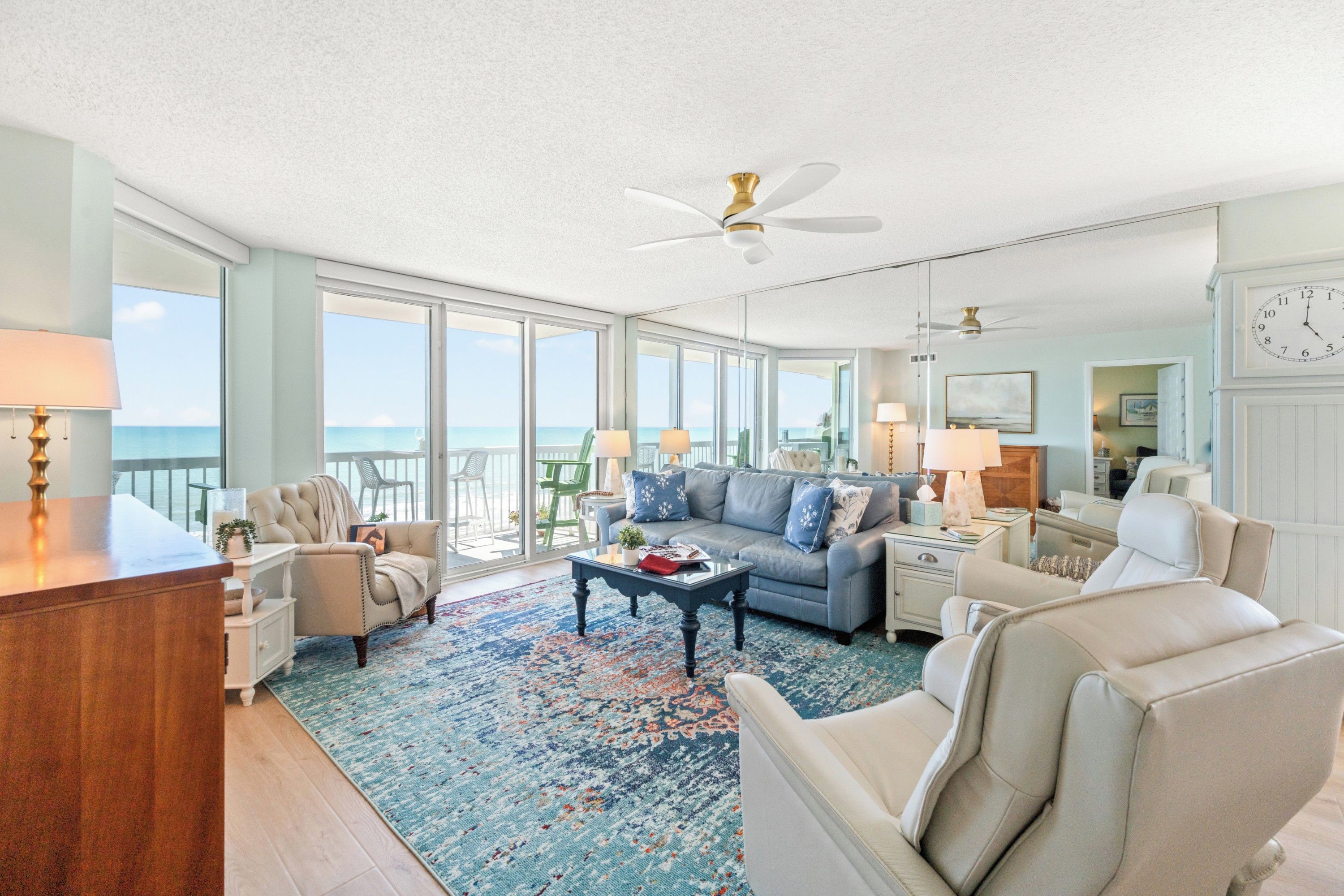 A spacious living room with a large window overlooking the ocean, a ceiling fan, and a clock on the wall.